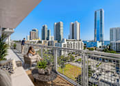 Thumbnail 1 of 76 - A woman is sitting on a balcony with a view of a city skyline.