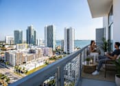 Thumbnail 68 of 76 - Two people sitting on a balcony overlooking a cityscape.