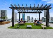 Thumbnail 9 of 76 - A man and woman are sitting on a couch under a pergola on a rooftop patio.