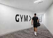 Thumbnail 20 of 76 - A man walking in a hallway with a Gym sign on the wall.