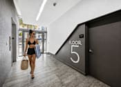 Thumbnail 19 of 76 - A woman is walking down a hallway carrying a brown bag and shopping bags.