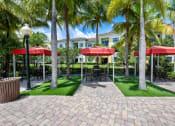 Thumbnail 10 of 44 - a courtyard with red umbrellas and green grass and palm trees