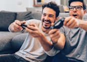 Thumbnail 3 of 7 - Two men are playing video games on a couch.