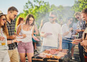 Thumbnail 5 of 7 - A group of people are gathered around a barbecue grill, enjoying a sunny day outdoors.