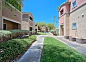 Thumbnail 3 of 16 - A sunny day in a residential area with apartment buildings and a sidewalk.