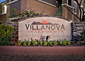 Thumbnail 7 of 16 - A sign for Villanova Apartments is surrounded by plants and flowers.