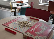 Thumbnail 20 of 50 - A Scrabble board game is set up on a table in a room with chairs at Denver Metro Village Apartments, Colorado