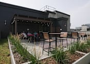 Thumbnail 15 of 50 - A modern outdoor seating area with a bar and people sitting at tables at Denver Metro Village Apartments, Denver, 80204