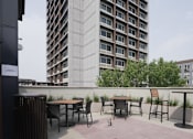 Thumbnail 9 of 50 - A patio with a table and chairs overlooks a tall building at Denver Metro Village Apartments, Denver, Colorado