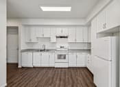 Thumbnail 23 of 42 - A white kitchen with wooden floors and white appliances.