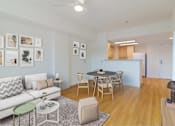 Thumbnail 2 of 17 - A living room with a white couch, a dining table with chairs, and pictures on the wall.