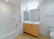 Thumbnail 7 of 17 - A white bathroom with a wooden cabinet and a white toilet.