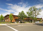 Thumbnail 1 of 11 - A large building with a brown roof and a tree in front of it.