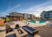 Thumbnail 3 of 26 - A modern outdoor seating area with a fire pit in the middle of a poolside patio.