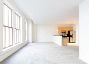 Thumbnail 13 of 32 - an empty living room with large windows and a kitchen in the background at 26 West, Managed by Buckingham Urban Living, Indianapolis