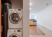 Thumbnail 14 of 32 - a washer and dryer in a laundry room with a kitchen in the background at 26 West, Managed by Buckingham Urban Living, Indianapolis