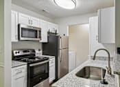 Thumbnail 76 of 107 - A kitchen with a black refrigerator, white cabinets, and a granite countertop.