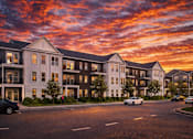Thumbnail 2 of 10 - A modern apartment building with cars parked in front.