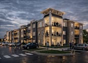 Thumbnail 4 of 8 - A large apartment building with balconies and multiple cars parked in the parking lot.
