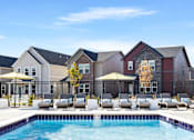 Thumbnail 26 of 37 - A pool area with lounge chairs and umbrellas in front of a row of houses.