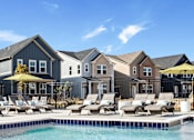 Thumbnail 27 of 37 - A pool with lounge chairs and umbrellas in front of a row of houses.