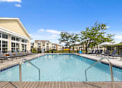 Thumbnail 31 of 34 - Sparkling swimming pool at Center Point Apartments with surrounding sun deck, lounge chairs, and views of the leasing office and buildings.