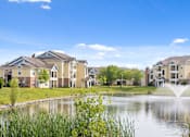 Thumbnail 33 of 34 - Wide-angle view of the tranquil pond and water feature surrounded by yellow apartment buildings and manicured green spaces at Center Point.