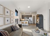 Thumbnail 9 of 27 - Model apartment living room with modern sofa, curated wall art, open kitchen with island seating, stainless steel appliances, and contemporary finishes at Montage