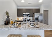 Thumbnail 1 of 27 - Model apartment kitchen at Montage West Lafayette featuring granite countertops, stainless steel appliances, modern cabinetry, and a large kitchen island with seating.