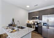 Thumbnail 2 of 27 - Modern apartment kitchen with granite island, stainless steel appliances, dark cabinetry, and undermount sink at Montage apartment community