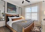 Thumbnail 5 of 27 - Model apartment bedroom at Montage West Lafayette featuring a modern bed frame, layered bedding, ceiling fan, and large window with natural light.