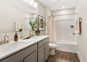 Thumbnail 6 of 45 - Contemporary apartment bathroom at Mural Lewis Center featuring double sink vanity, quartz countertops, large mirror, tub shower combination, and wood-style flooring