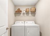 Thumbnail 34 of 45 - Laundry room in single-family rental home at Mural Lewis Center featuring full-size washer and dryer, overhead shelf storage, and clean, modern design