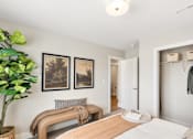 Thumbnail 20 of 45 - Stylish apartment bedroom at Mural Lewis Center featuring neutral tones, ceiling fan, large window, framed wall art, and modern furnishings with natural light