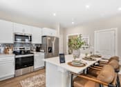Thumbnail 1 of 45 - Open-concept apartment kitchen at Mural Lewis Center featuring large island with seating, white cabinetry, stainless steel appliances, subway tile backsplash, and wood-style flooring