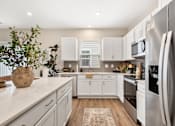 Thumbnail 3 of 45 - Bright modern apartment kitchen at Mural Lewis Center featuring white shaker cabinets, quartz countertops, stainless steel appliances, kitchen island, and wood-style flooring