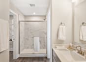 Thumbnail 9 of 45 - Spacious apartment bathroom at Mural Lewis Center featuring glass-enclosed walk-in shower, double sink vanity, large mirror, modern lighting, and wood-style flooring