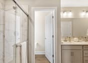 Thumbnail 11 of 45 - Modern bathroom in single-family rental home at Mural Lewis Center featuring glass walk-in shower, dual sink vanity, bright lighting, and wood-style flooring