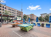 Thumbnail 60 of 68 - A sunny day in a city square with a green and yellow table in the center.