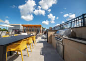 Thumbnail 32 of 36 - a patio with a grill and tables with yellow chairs at The Century at Purdue Research Park-Student, West Lafayette, 47906