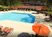 Thumbnail 11 of 21 - a swimming pool with chairs and an umbrella in a garden at Landmark at Lyncrest Reserve Apartments, Nashville, TN, 37209