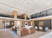 Thumbnail 12 of 38 - Expansive apartment leasing office featuring soaring double-height ceilings, a modern reception desk, cozy resident lounge seating, and massive windows that fill the space with beautiful natural light.