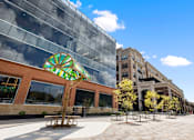 Thumbnail 28 of 38 - Exterior view of the Portrait Midtown apartment community featuring modern architectural design, a bright outdoor patio with comfortable seating, and colorful umbrellas.