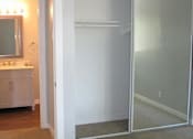Thumbnail 4 of 16 - An empty bedroom with tan carpets and a sliding mirror doors to the closet. The bathroom is barely visible to the right.