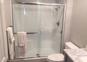 Thumbnail 14 of 16 - The bathroom with a tub & shower combo that has glass doors. A towel lays on the bar of the door. The toilet is in middle and a sink barely visible on the right
