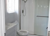 Thumbnail 16 of 16 - The bathroom with a tub & shower combo that has glass doors. The toilet is in front with a window of light behind and a sink on the left.