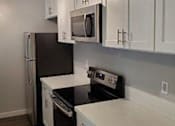Thumbnail 9 of 16 - A kitchen with stainless steel appliances including a microwave, an oven and stove, and fridge. The cabinets are all white with chrome handles.
