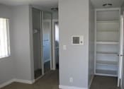 Thumbnail 12 of 16 - A large empty bedroom looks down the hallway lined with closets to the entryway into the bathroom. Shelving is on the right side where the door opens to the bedroom.