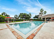 Thumbnail 4 of 10 - A large swimming pool with a red tile border and a building in the background.