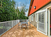 Thumbnail 34 of 74 - A wooden deck with a table and chairs is surrounded by greenery.